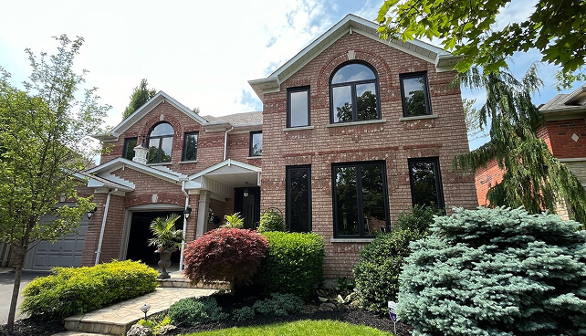 Custom multi-pane architectural windows and a dark front entry door on a luxury stone home exterior.