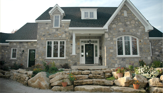 Custom multi-pane architectural windows and a dark front door on a luxury stone home facade.