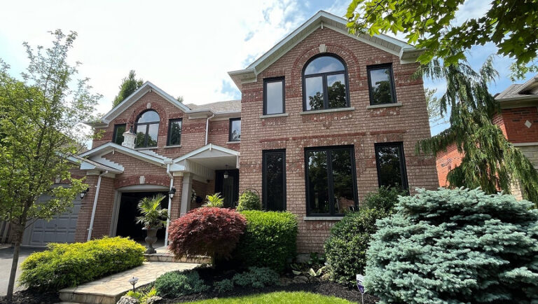 Custom multi-pane architectural windows and a dark front entry door on a luxury stone home exterior.